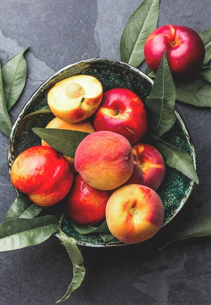 Fresh ripe peach with peach tree leaves in green bowl top view