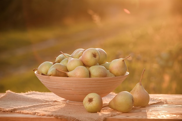 日没の自然の果樹園の背景を持つ木製のテーブルのバスケットに新鮮な熟した梨。ベジタリアン フルーツ組成。収穫のコンセプト