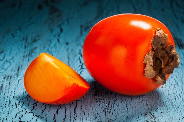 Fresh ripe persimmon with slice on a blue wooden background