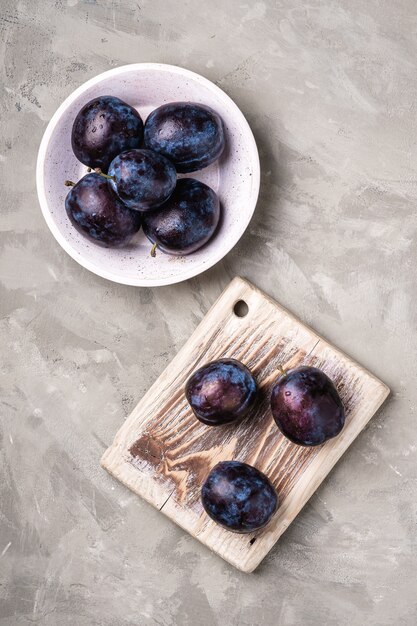 Fresh ripe plum fruits with water drops in wooden bowl and cutting board