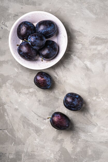 Fresh ripe plum fruits with water drops in wooden bowl on stone concrete , top view