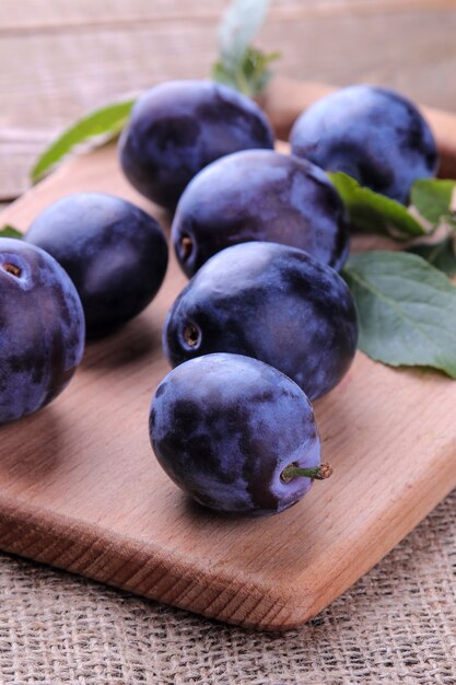 Fresh ripe plums with leaves on a board on a brown wooden table