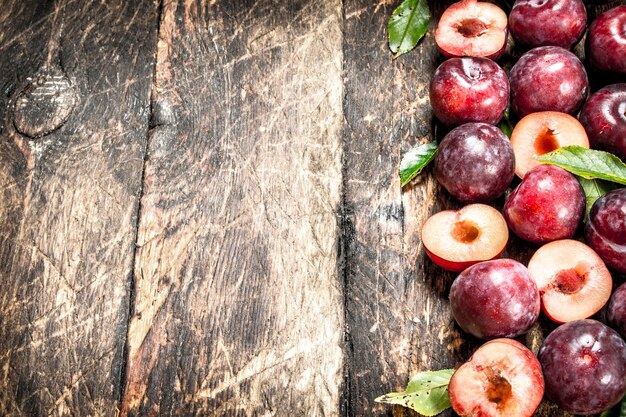 Fresh, ripe plums with leaves. On a wooden background.