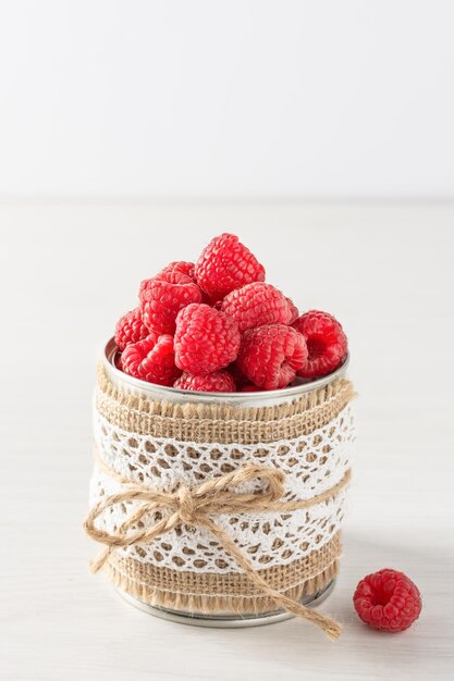 Fresh ripe raspberries in a metal small container on white wooden table