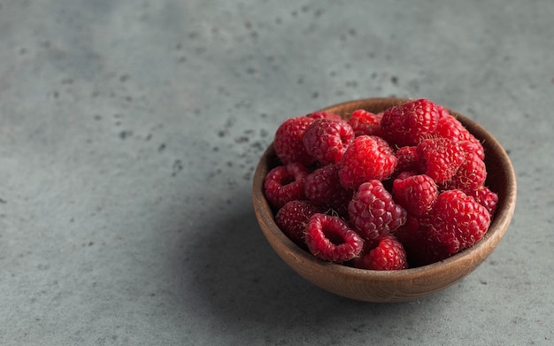 Fresh ripe raspberries in a wooden bowl on gray