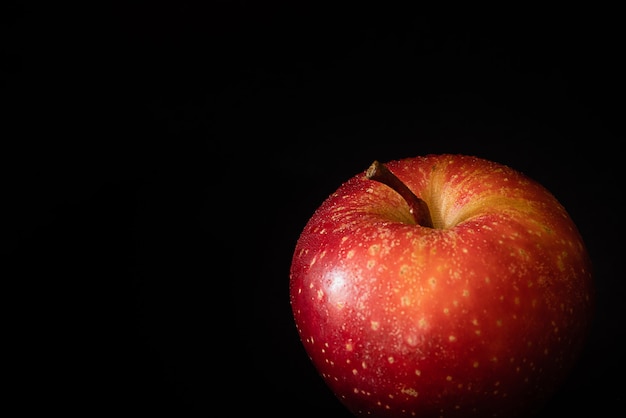 Fresh ripe red apple with water drops on glossy peel on black surface