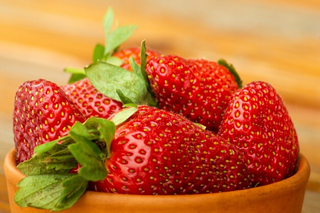 Fresh ripe red strawberries in a clay bowl on an old wooden table, outdoor, close up.