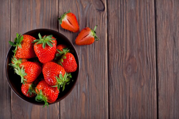 Fresh ripe strawberries in a brown bowl on a brown wooden background