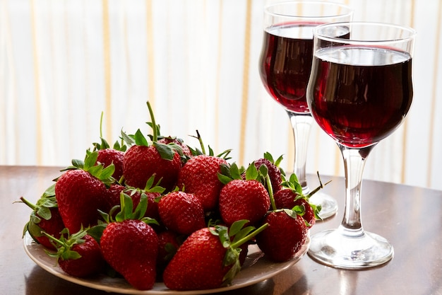 Fresh ripe strawberries and glasses of red wine in the background