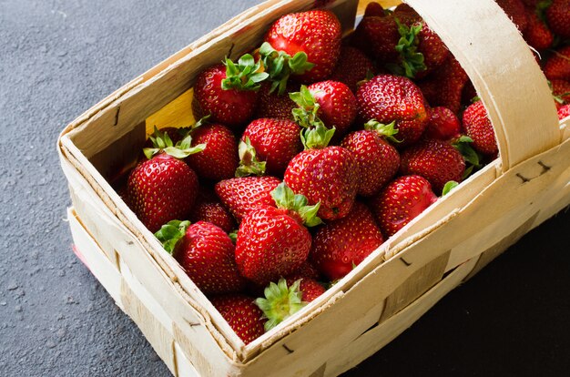 Fresh ripe strawberries in a wooden basket on a dark background. Organic juicy berries.