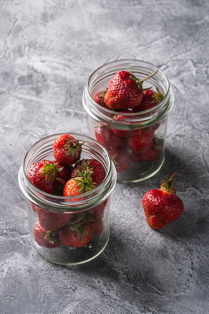 Fresh ripe strawberry fruits in two glass jars, summer vitamin berries on grey stone table, angle view