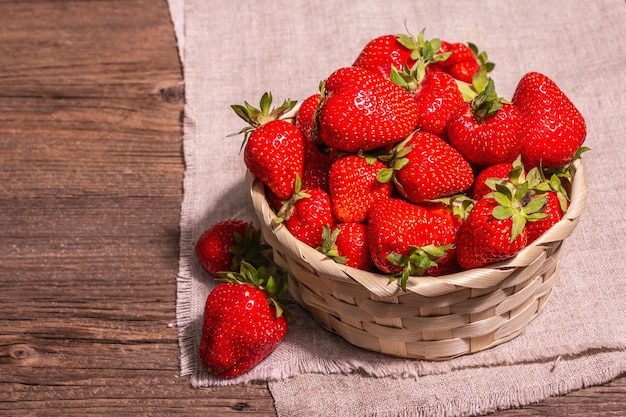 Fresh ripe strawberry in a wicker basket. Sweet summer fruit, healthy food. Modern hard light, dark shadow. Vintage wooden boards background