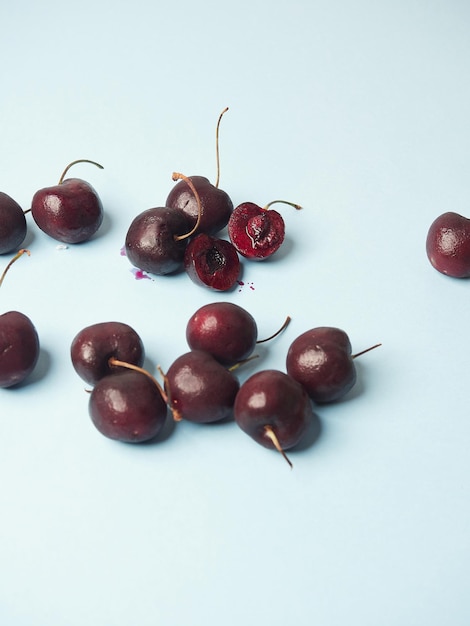 Fresh ripe sweet cherries on a blue surface one split in half showing its juicy purple interior flesh with seed