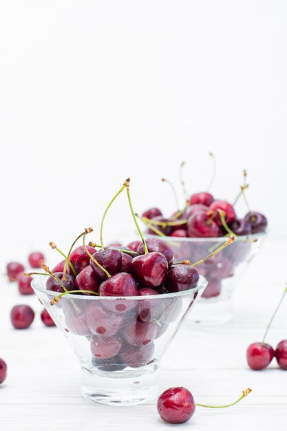 Fresh ripe sweet cherries in water drops in bowls on a white wooden table. Copy space