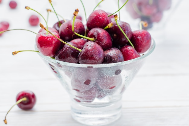 Fresh ripe sweet cherries in water drops in glass bowl on a white wooden table