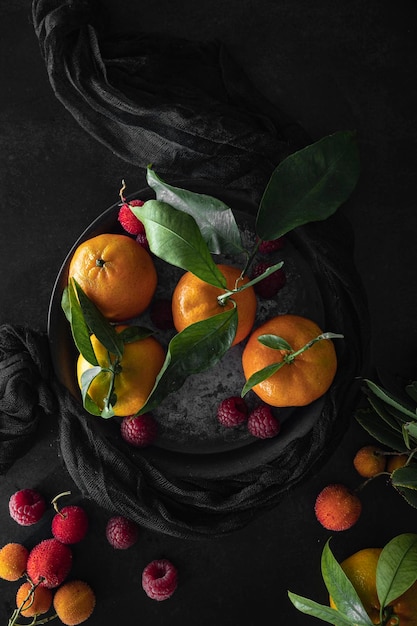 Photo fresh, ripe tangerines with green leaves and raspberries on a dark background