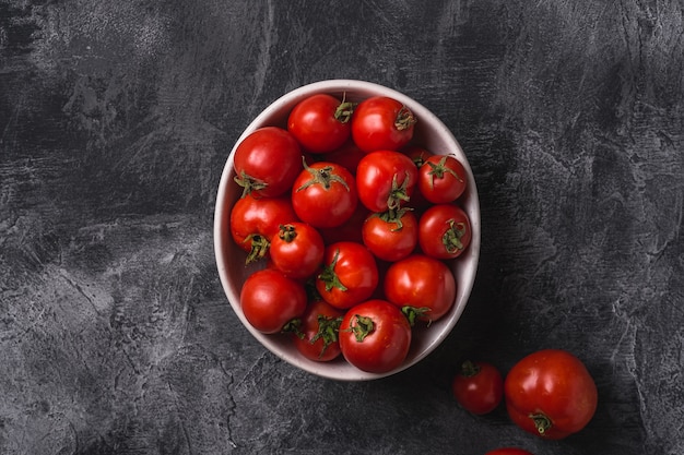 Fresh ripe tomatoes in bowl on dark concrete surface, top view