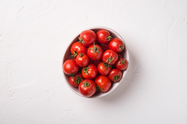 Fresh ripe tomatoes in bowl on white concrete surface