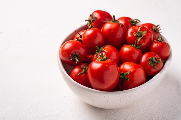 Fresh ripe tomatoes with water drops in bowl on white concrete