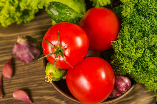 Fresh ripe tomatoes on a wooden table with a green salad on the background Fresh vegetables Delicious vegetarian food Salad