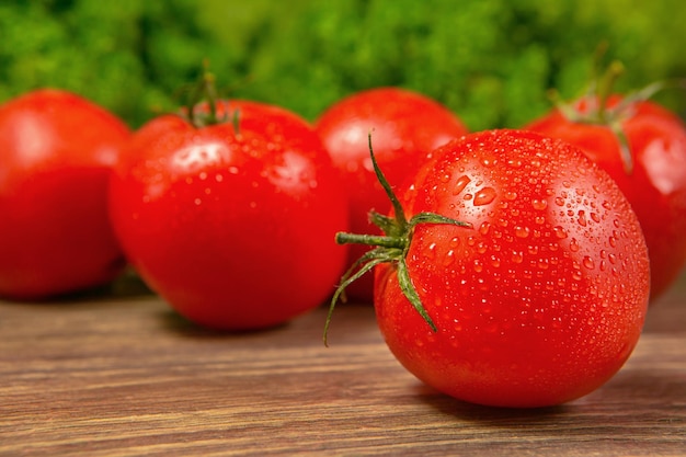 Fresh ripe tomatoes on a wooden table with a green salad on the background Fresh vegetables