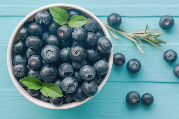 Fresh ripe wild blueberries in white bowl on blue wood table 