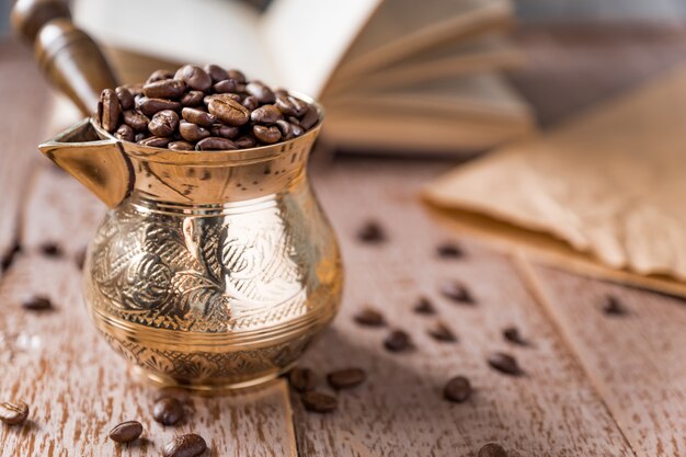 Fresh roasted coffe beans in  cezve (traditional turkish coffee pot) and opened book on wooden table.