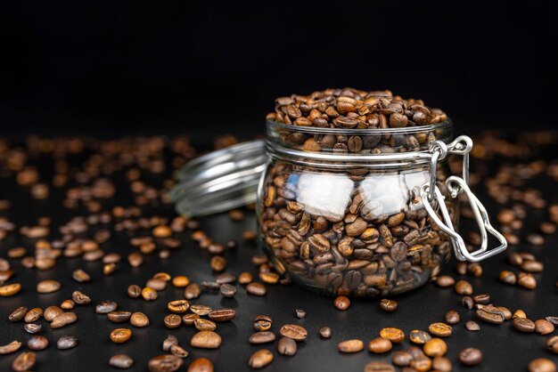 fresh roasted coffee beans in a open transparent jar standing on a black table with lots of coffee