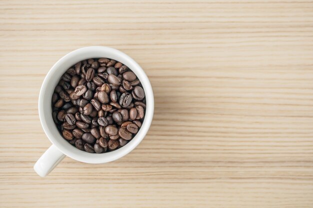 Fresh roasted coffee beans in white cup on wood table, top view