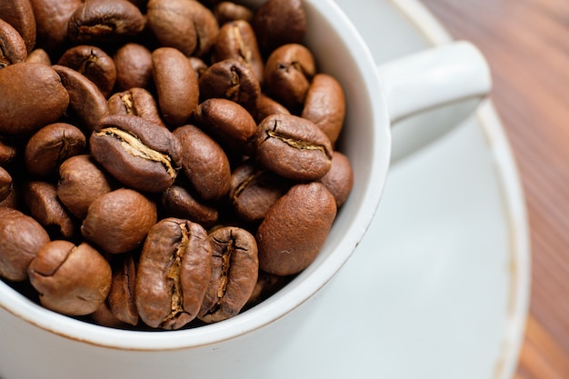 Fresh roasted coffee beans in white mug on brown wood.