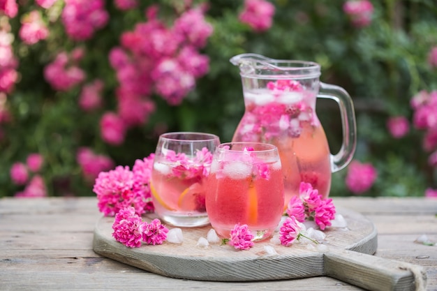 Fresh rose lemonade with ice and fresh roses over natural garden