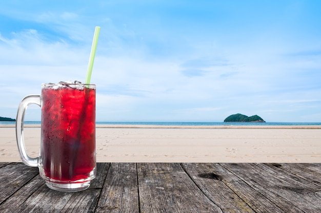 新鮮なロゼルジュースの甘い水と氷のグラスアイスコーヒー、ビーチの風景を望む木製のテーブル、自然の背景、夏の健康ドリンク、氷