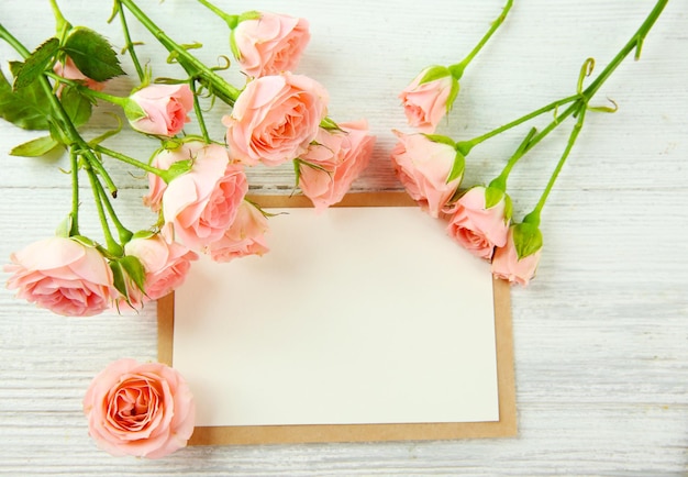 Fresh roses and photo frame on wooden background