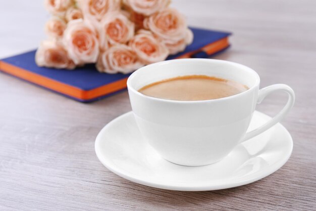 Fresh roses with diary and cup of coffee on wooden background