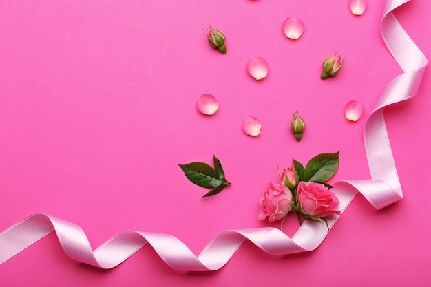 Fresh roses with ribbon on pink background