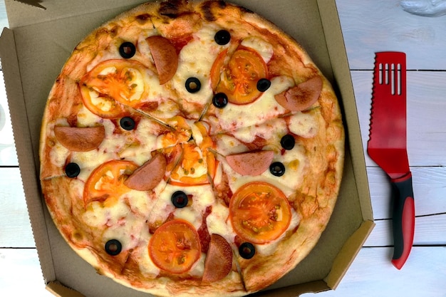 Fresh round pizza with tomatoes sausage mozzarella and olives in cardboard box