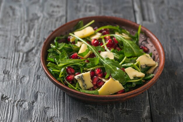 Fresh salad of arugula, pomegranate and blue cheese on a wooden table. Diet vegetarian salad.