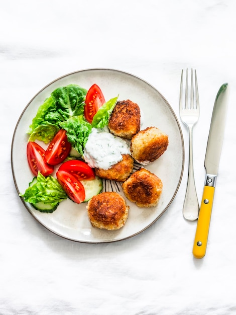 Fresh salad and canned tuna potato fish balls with greek yogurt cilantro sauce on light background top view