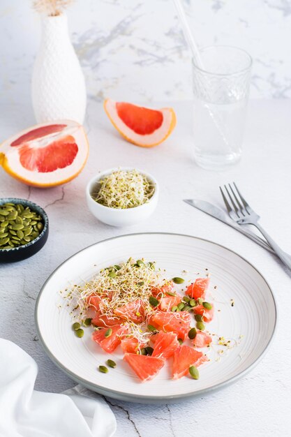 Fresh salad of grapefruit clover and alfalfa sprouts and pumpkin seeds and cutlery on a plate on the table Organic vegetarian detox food Vertical view