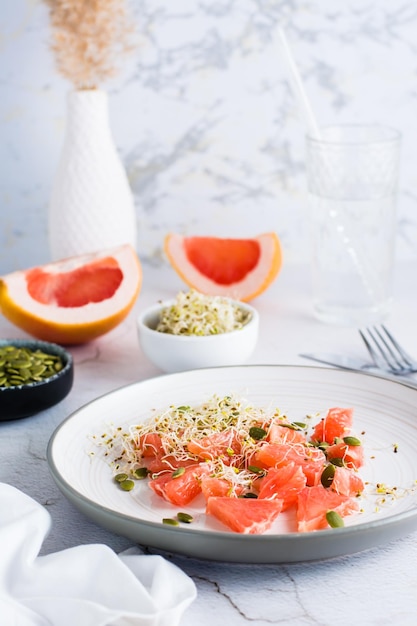 Fresh salad of grapefruit clover and alfalfa sprouts and pumpkin seeds on a plate on the table Organic vegetarian detox food Vertical view