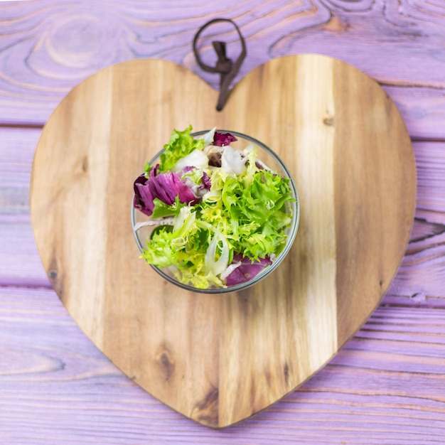 A fresh salad of greens on a wooden background in the form of a heart Vegetarian food Diet