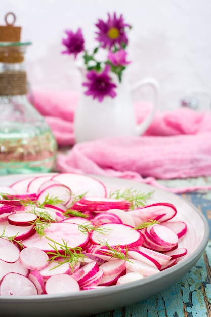 Fresh salad of pieces of radish and dill on a plate on a wooden table