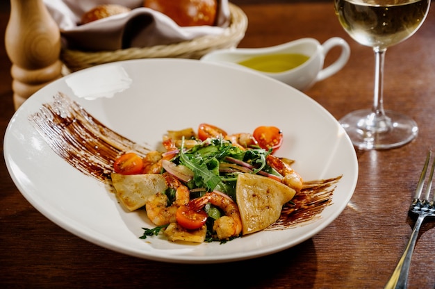 Fresh salad plate with shrimp, tomato and mixed greens on wooden surface close up