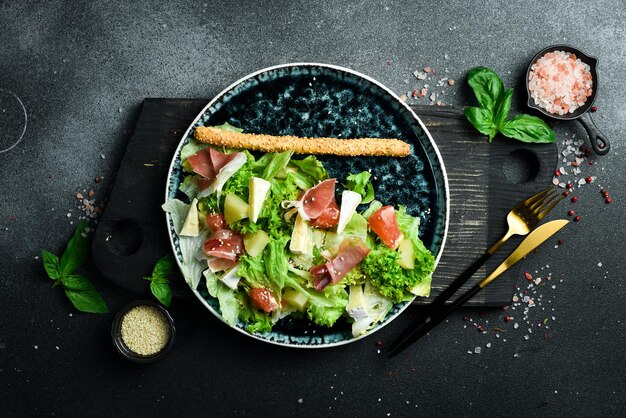 Фото Свежий салат, прошутто, сыр и ананас на темном фоне.