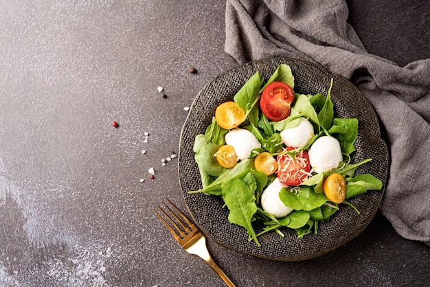 Fresh salad with arugula cherry tomatoes mozzarella cheese and hard cheese on dark background Top view