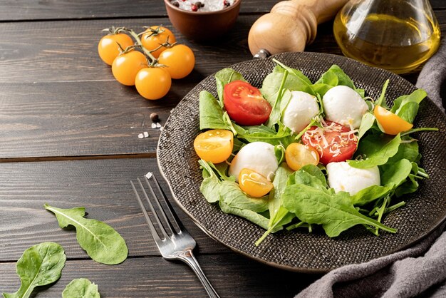 Fresh salad with arugula cherry tomatoes mozzarella cheese and hard cheese on dark wooden background Top view