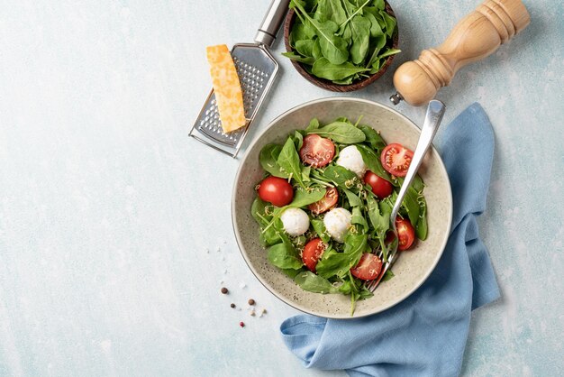 Fresh salad with arugula cherry tomatoes mozzarella cheese and hard cheese on white wooden background Top view