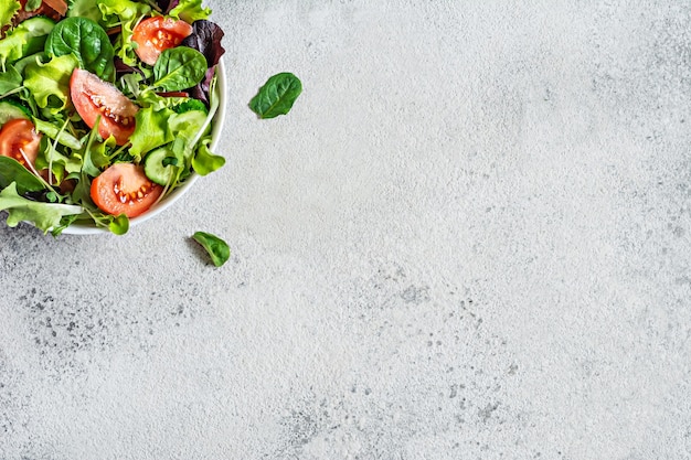 Fresh salad with fresh vegetables ripe tomatoes cucumber lettuce and microgreen  in a bowl on a gray background Healthy raw food concept Place for text copy space