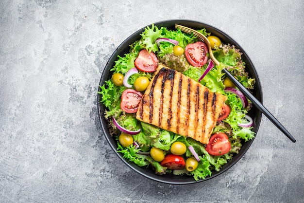 Fresh salad with grilled cheese tomatoes and olives on grey