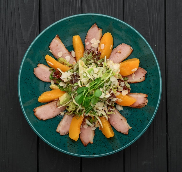 Fresh salad with grilled meat, caramelized peach and vegetables on a black